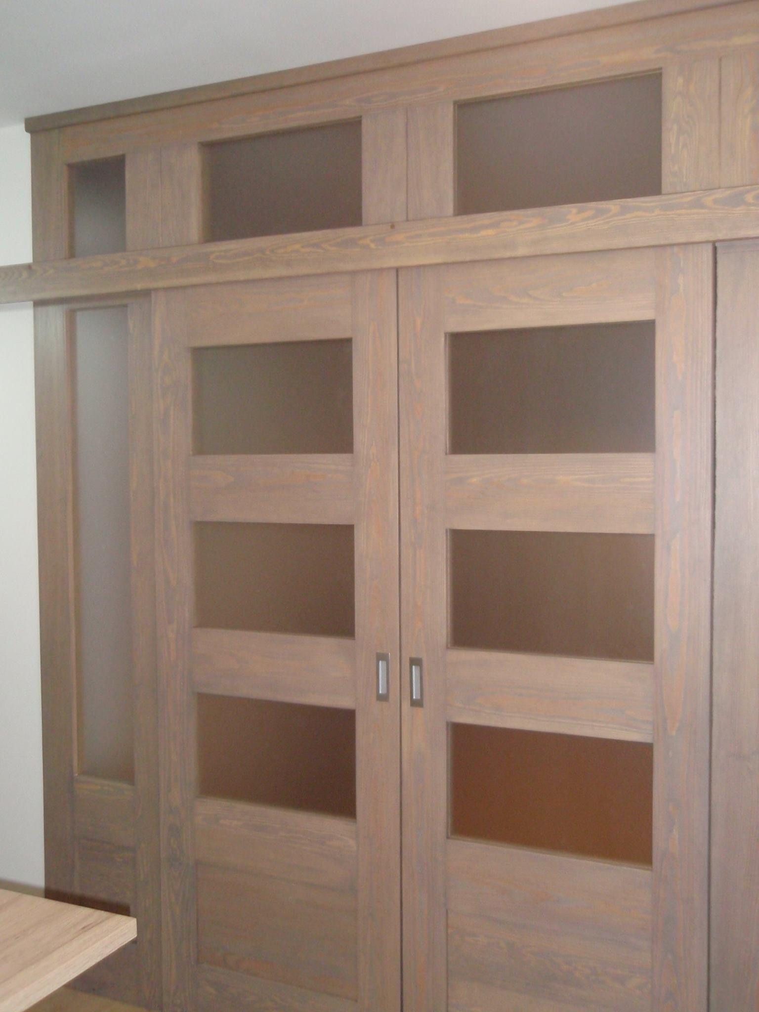 Drewniana szafa przesuwna z górną nadstawką i matowymi szybami w drzwiach, wykończona w odcieniach brązu z widocznym usłojeniem drewna.