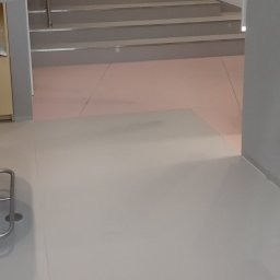 Gładzix Hubert Wójcik - Jasnoszara podłoga z płytek ceramicznych przechodząca w schody w nowoczesnym wnętrzu, widok na klatkę schodową z boku.