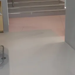 Jasnoszara podłoga z płytek ceramicznych przechodząca w schody w nowoczesnym wnętrzu, widok na klatkę schodową z boku.