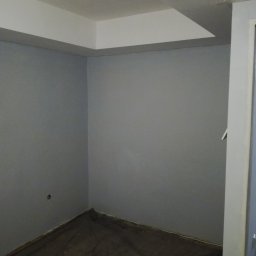 Gładzix Hubert Wójcik - Szare ściany w pokoju z zabezpieczoną folią podłogą, przygotowane do malowania lub remontu, z widocznym narożnikiem sufitu z podwieszaną konstrukcją.