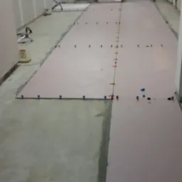 Przygotowanie podłoża pod panele podłogowe z użyciem pianki izolacyjnej i dystansów, widoczne surowe ściany w trakcie wykończenia.