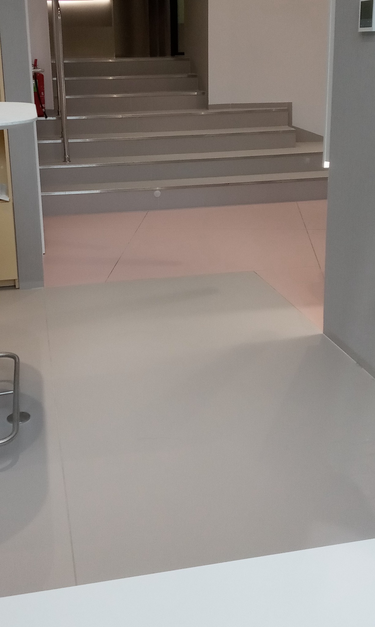 Jasnoszara podłoga z płytek ceramicznych przechodząca w schody w nowoczesnym wnętrzu, widok na klatkę schodową z boku.