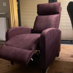 KORSA-MEBL - Rozłożony fotel relaksacyjny w odcieniach fioletu, z wysuwanym podnóżkiem, na drewnianej podłodze, w tle okno z żaluzjami i zasłoną.