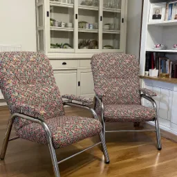 Dwa krzesła z chromowanymi ramami i tapicerką w geometryczny wzór, stojące na drewnianej podłodze na tle kredensu i regału z książkami.