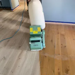 Parkiet częściowo wyszlifowany maszyną Hummel, widoczna różnica w kolorze i strukturze drewna, worek na pył w tle.