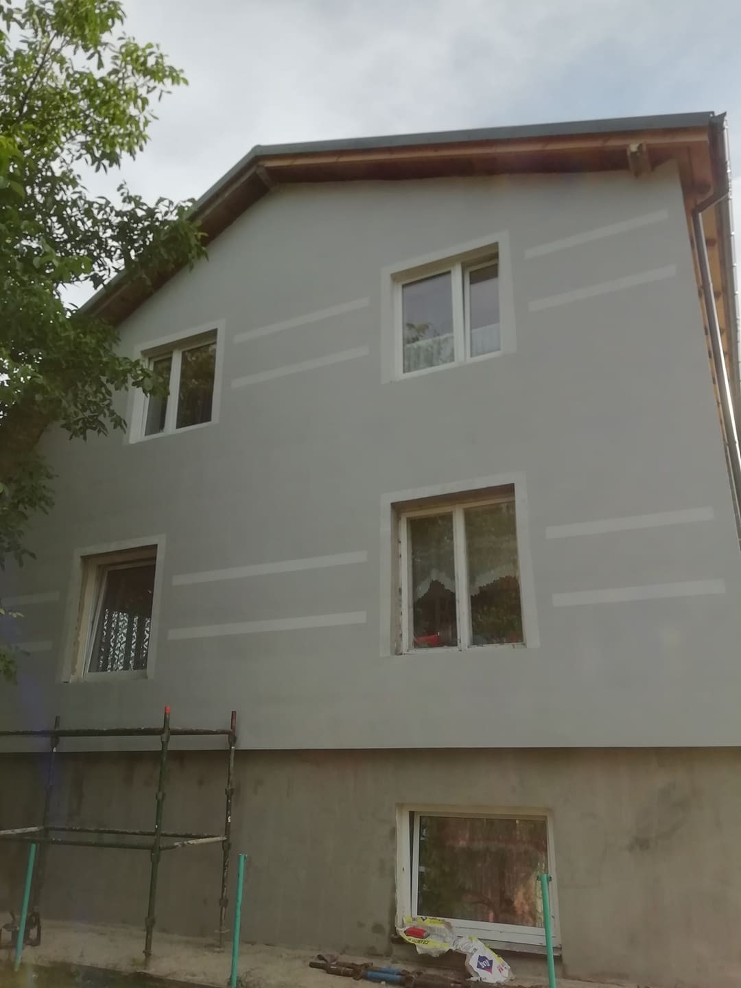 Dom w Malborku w trakcie nakładania warstwy izolacyjnej na elewacji, widoczne rusztowanie i białe pasy wyznaczające obszary do pokrycia.