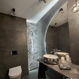 MAO Magdalena Owczarek - Nowoczesna łazienka z szarymi płytkami, podwieszaną toaletą i umywalką w kształcie misy. Dekoracyjna ściana z efektem marmuru podświetlona ledami. Lustro o nieregularnym kształcie z wbudowanym...