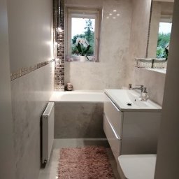 MAO Magdalena Owczarek - Jasna łazienka z wanną, umywalką w zabudowie i grzejnikiem, dekoracyjne płytki mozaikowe i puszysty dywanik.