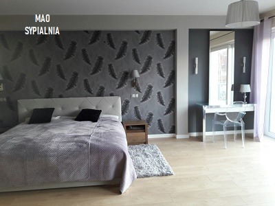 Sypialnia w odcieniach szarości z łóżkiem, toaletką z lustrem, ścianą w pióra i drewnianą podłogą.