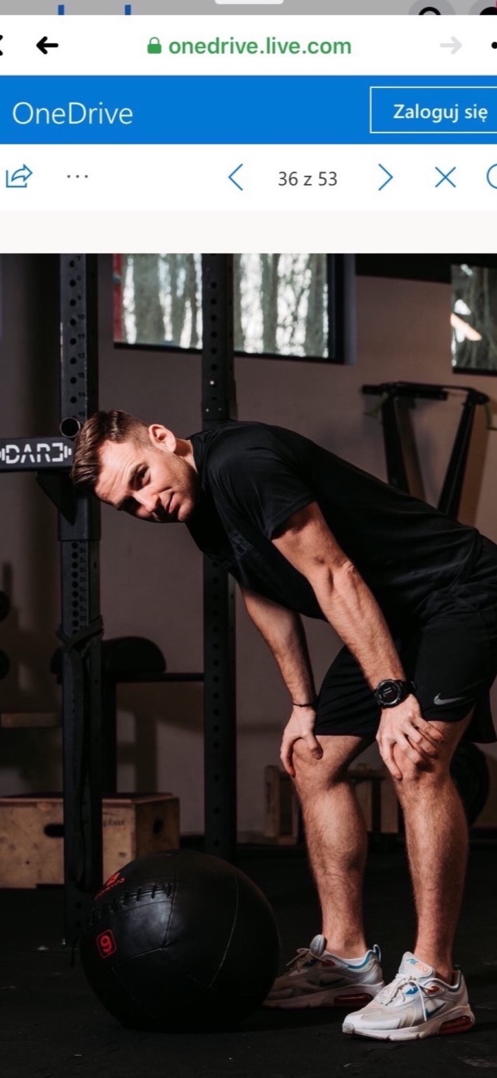 Mężczyzna w sportowym stroju opiera się na kolanach po intensywnym treningu z piłką lekarską w siłowni w Gdańsku.