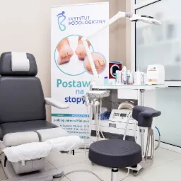 Gabinet podologiczny z fotelem do zabiegów, lampą i stolikiem z narzędziami, w tle baner reklamowy Instytutu Podologicznego.