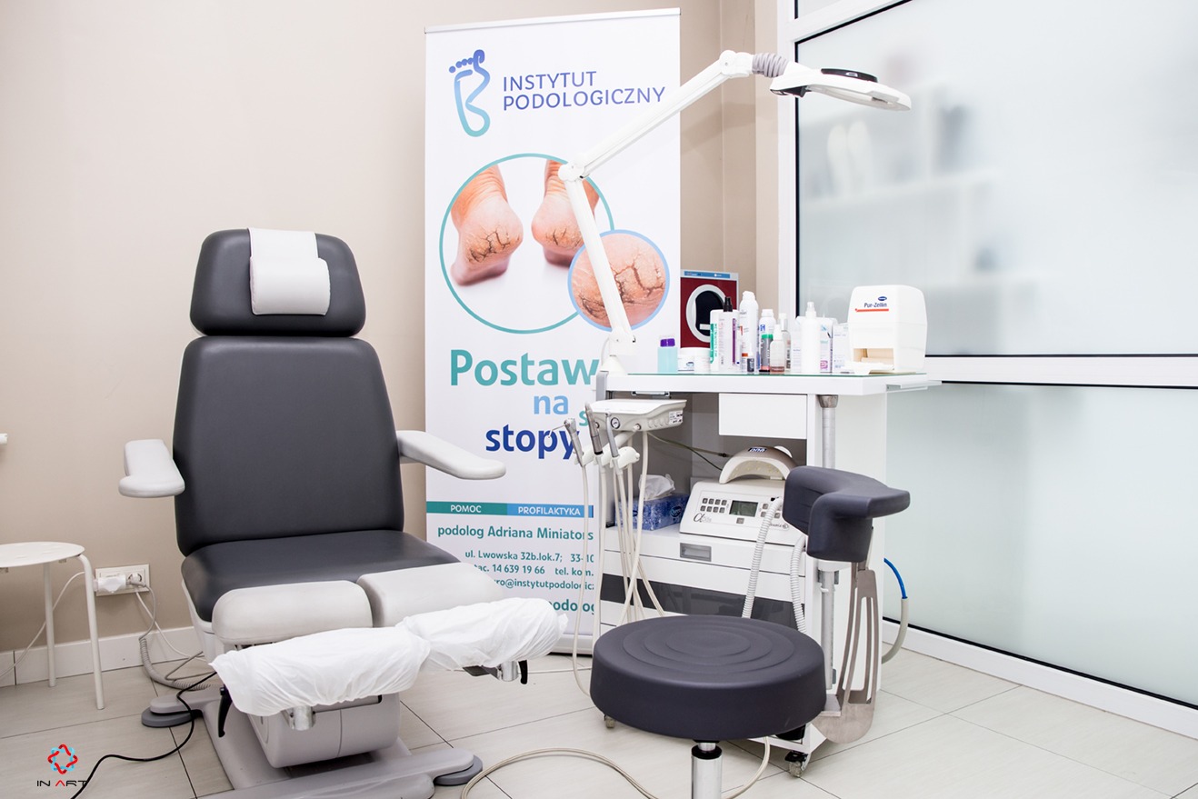 Gabinet podologiczny z fotelem do zabiegów, lampą i stolikiem z narzędziami, w tle baner reklamowy Instytutu Podologicznego.