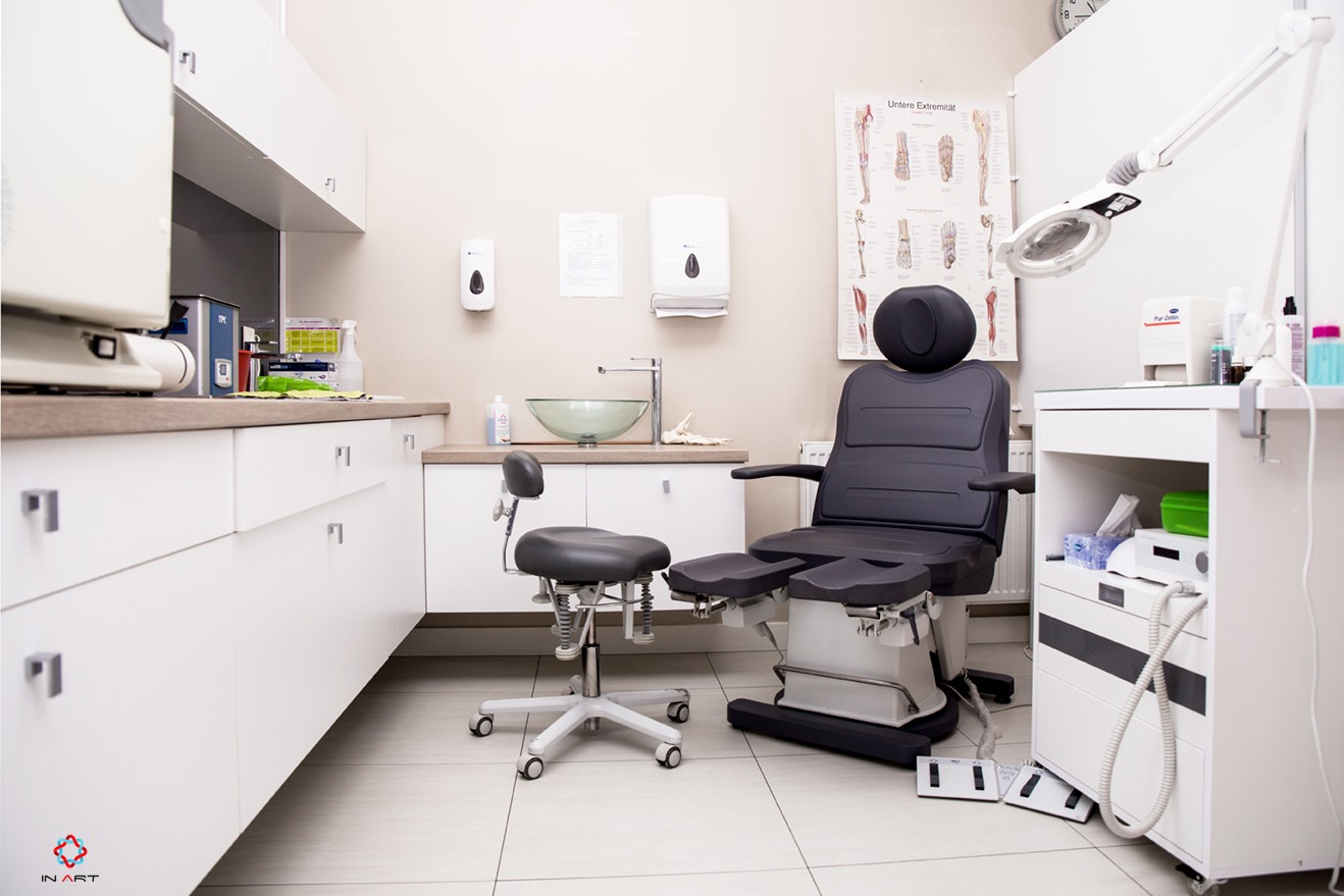 Nowoczesny gabinet kosmetyczny z fotelem do zabiegów, umywalką ze szklaną misą i plakatem anatomicznym kończyn dolnych.