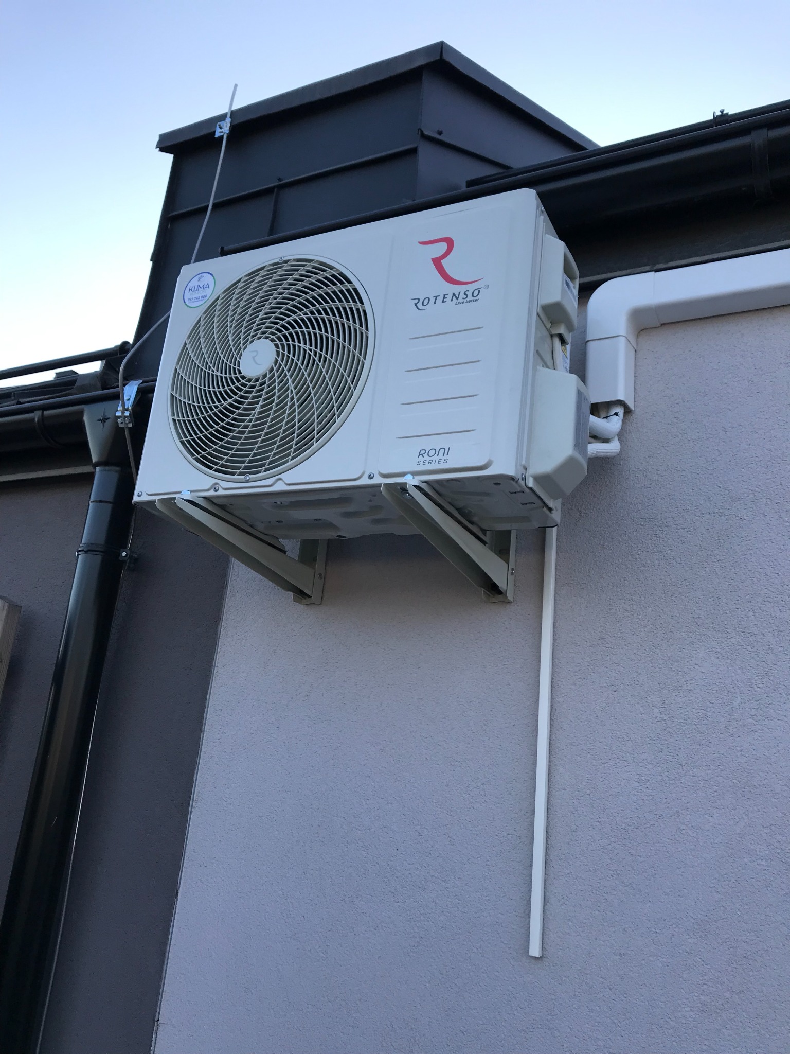 Zewnętrzna jednostka klimatyzacji Rotenso Roni 3,5kW zamontowana na elewacji budynku, widoczne orurowanie i odpływ skroplin.