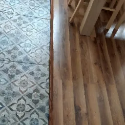 Połączenie płytek podłogowych z wzorem kwiatowym i paneli podłogowych imitujących drewno, widoczny fragment stołu i krzeseł.