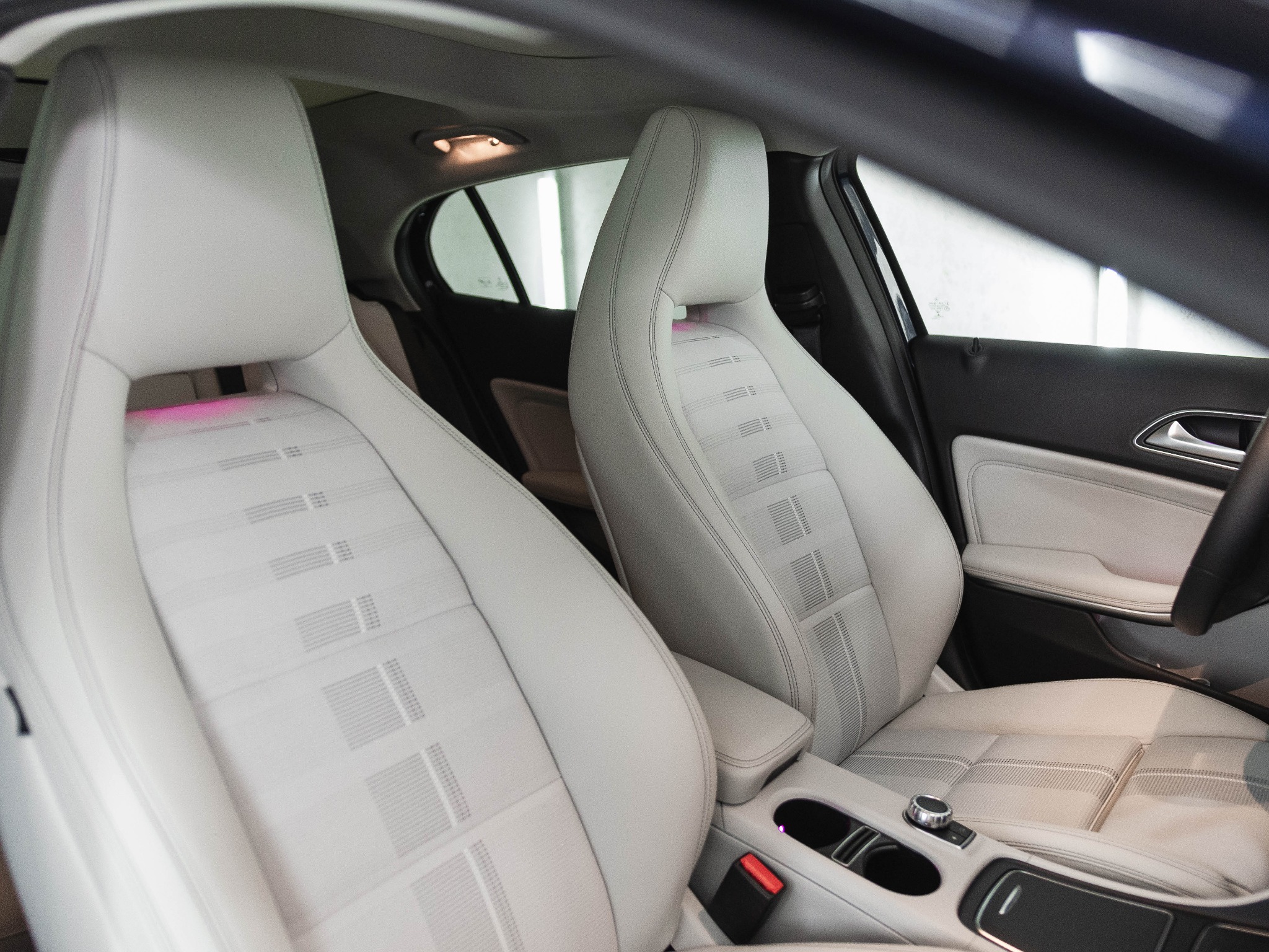 Jasnoszare, skórzane fotele przednie z subtelnym wzorem w nowym samochodzie, widoczne elementy deski rozdzielczej i czerwony pas bezpieczeństwa.