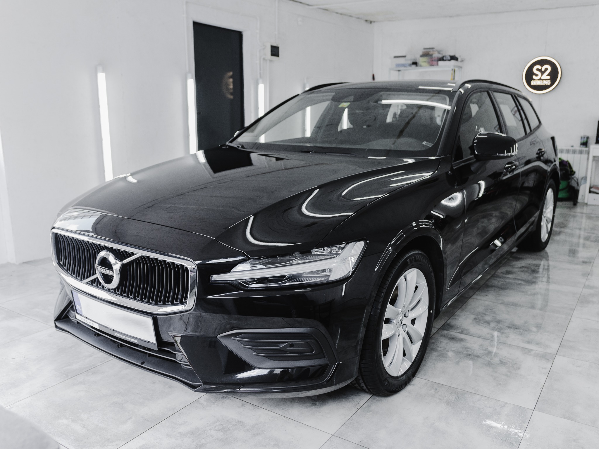 Błyszczący, czarny Volvo V60 po wizycie w myjni detailingowej, widoczne odbicia w lakierze, na podłodze czyste płytki, w tle logo S2 Detailing.