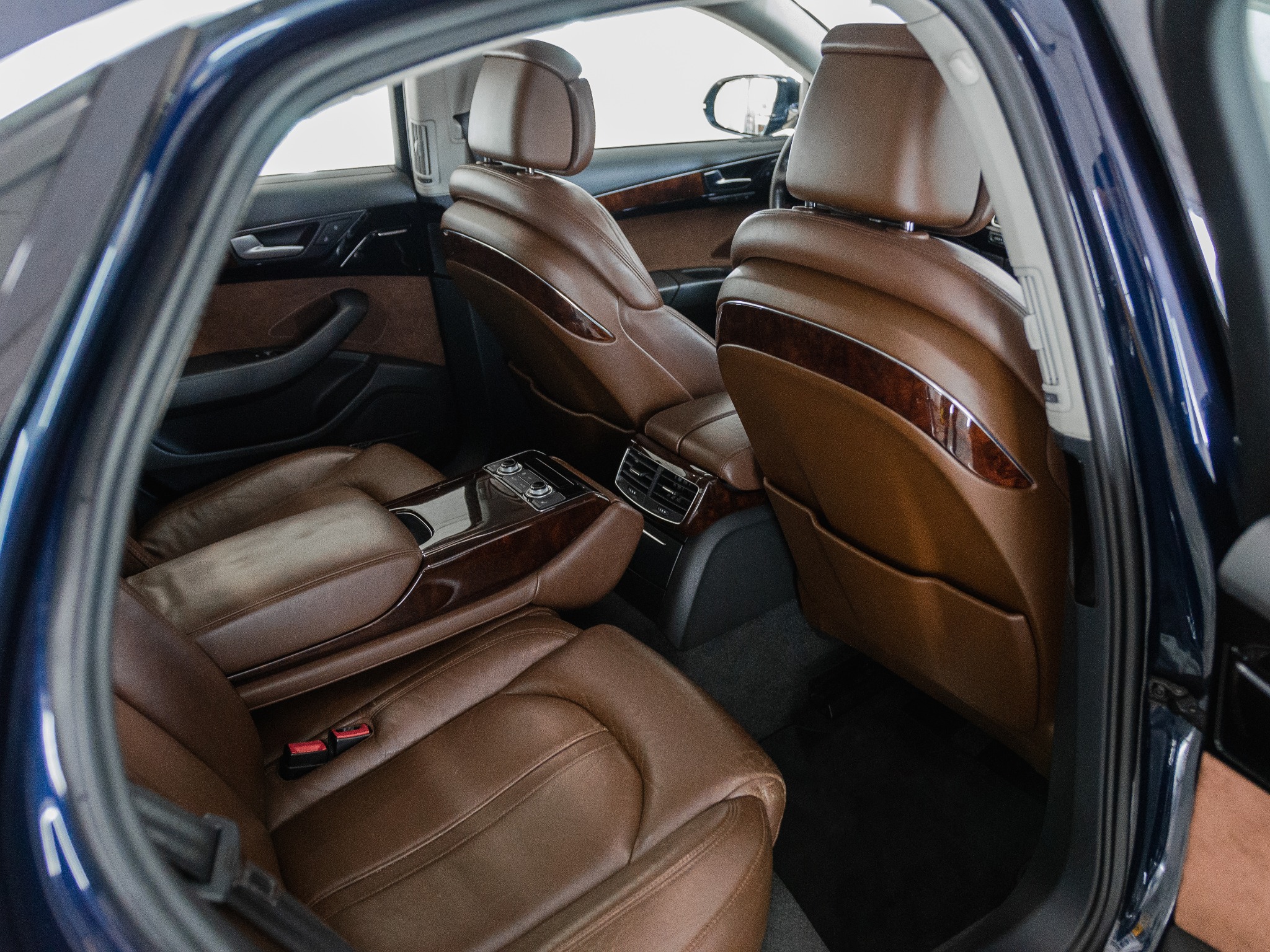 Wnętrze samochodu z brązową skórzaną tapicerką, widok z otwartych tylnych drzwi, ukazujący detale przeszyć i drewnianych elementów wykończenia.