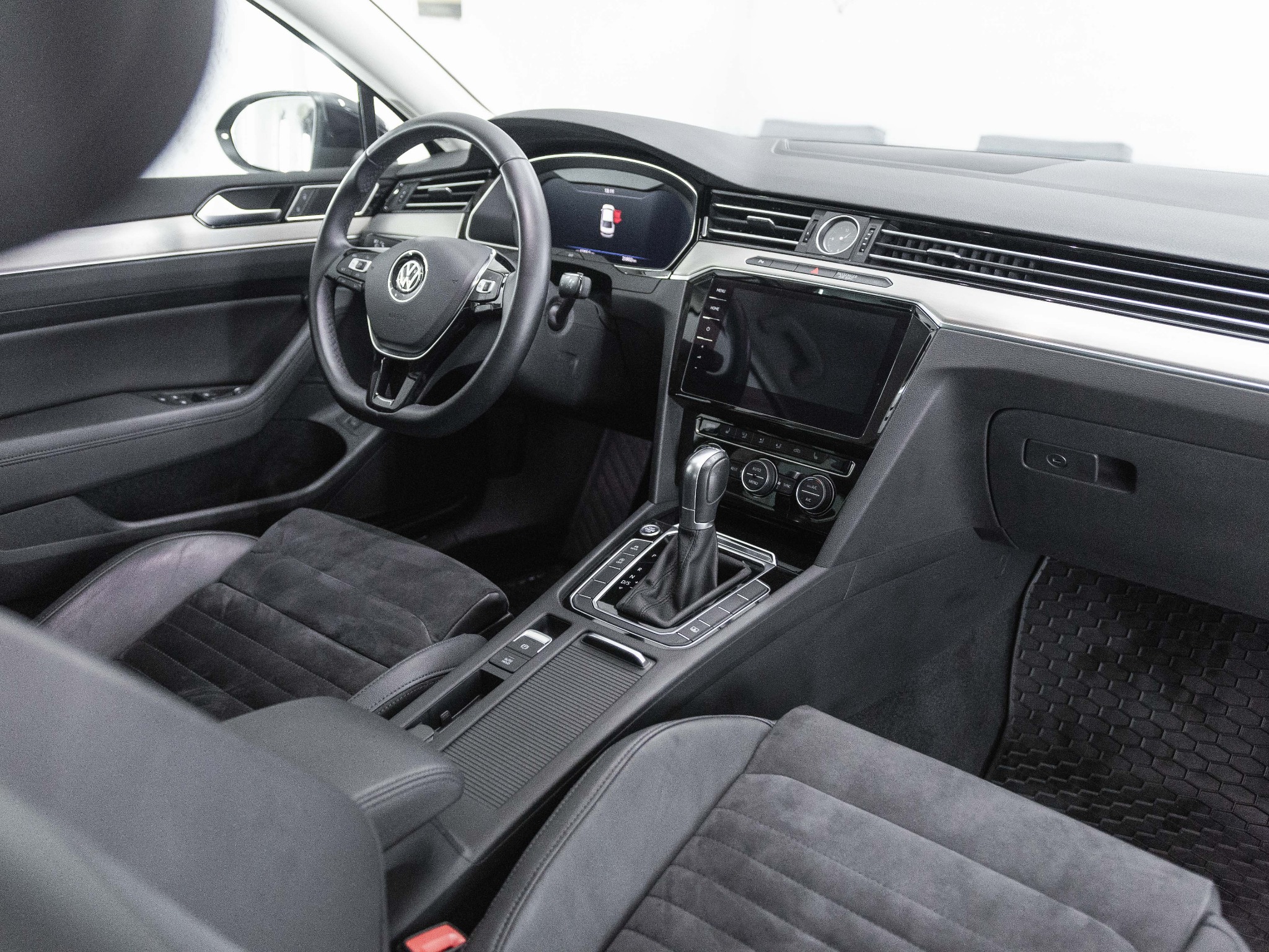 Wnętrze samochodu marki Volkswagen, widok na deskę rozdzielczą, kierownicę z logo, ekran nawigacji i dźwignię zmiany biegów; fotele z ciemnej alcantary.