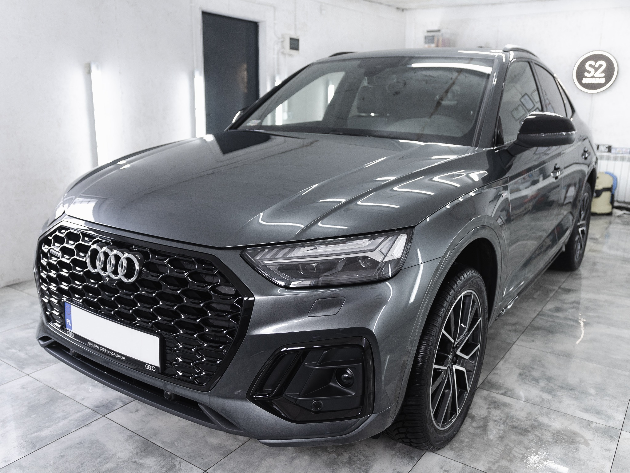 Szary Audi Q5 po umyciu, widoczny błyszczący lakier i czyste felgi, logo S2 Detailing w prawym górnym rogu.