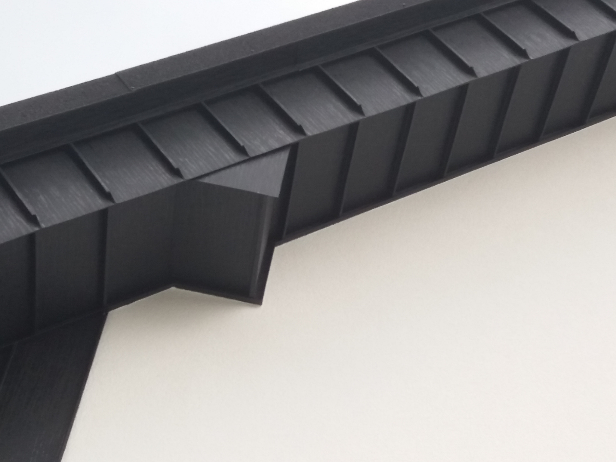 Nowoczesny, czarny okap dachu z metalu, z widoczną strukturą paneli, na tle jasnej ściany budynku.