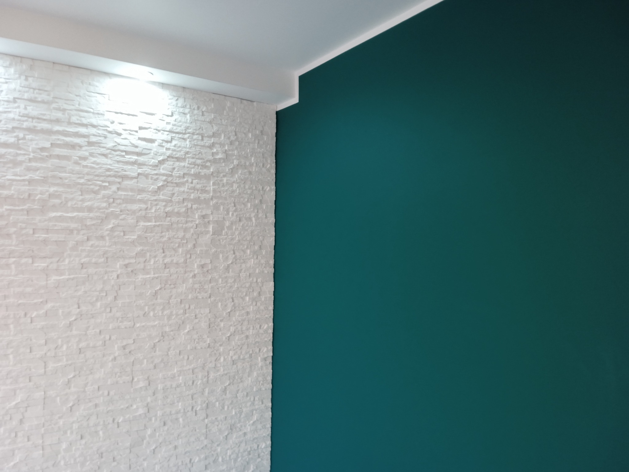 Ściana z białej, dekoracyjnej cegły sąsiadująca z gładką ścianą pomalowaną na kolor morski, widoczne białe listwy sufitowe.