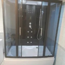 Kabina prysznicowa z hydromasażem, czarne ramy, biały brodzik, panel sterujący z dyszami, słuchawka prysznicowa na szynie, widok z przodu na tle jasnych płytek.