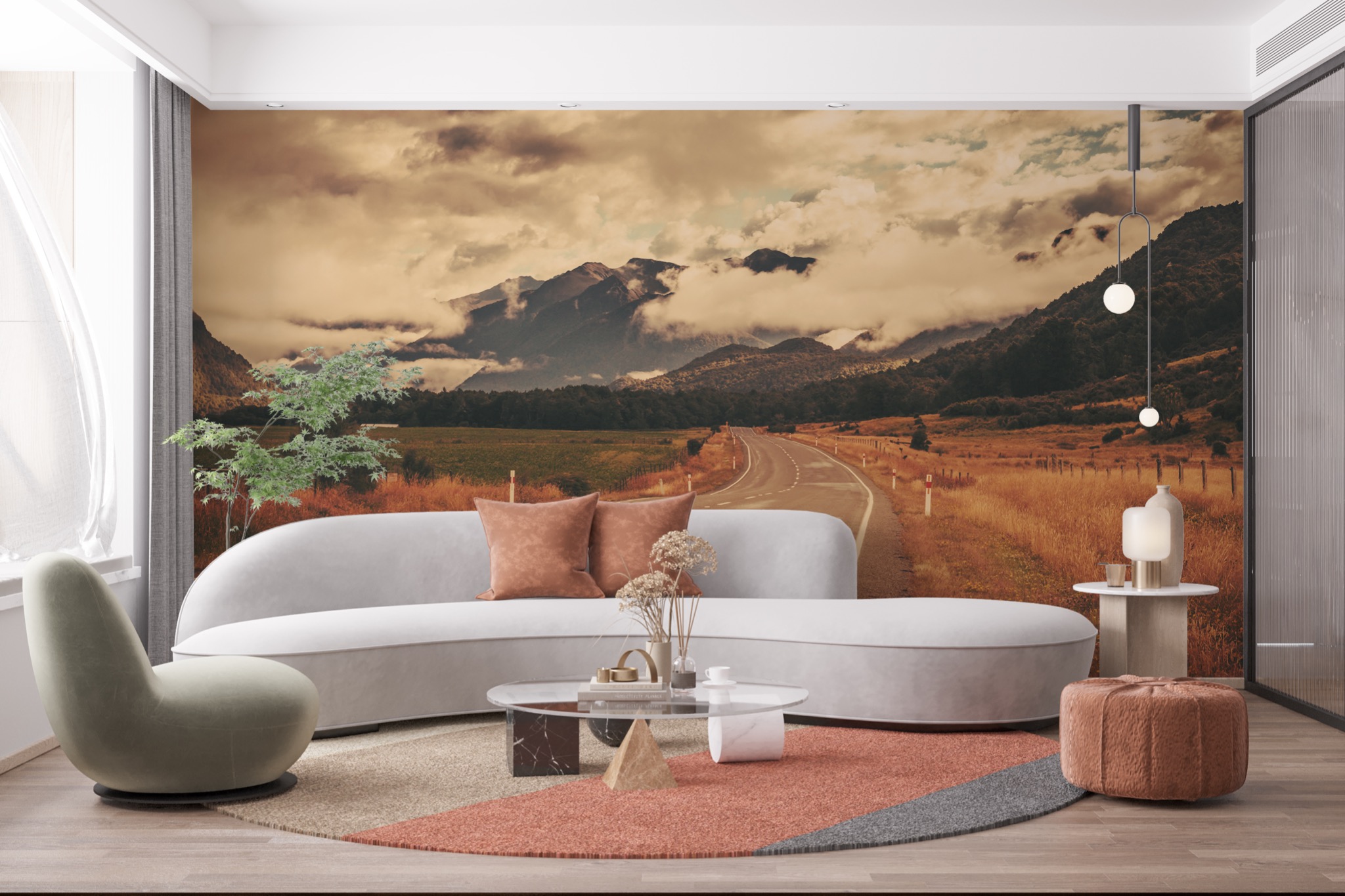 Wnętrze salonu z fototapetą przedstawiającą górski krajobraz z drogą, jasnoszara sofa z brązowymi poduszkami, okrągły stolik kawowy, oliwkowy fotel i lampa wisząca z dwoma kulami.