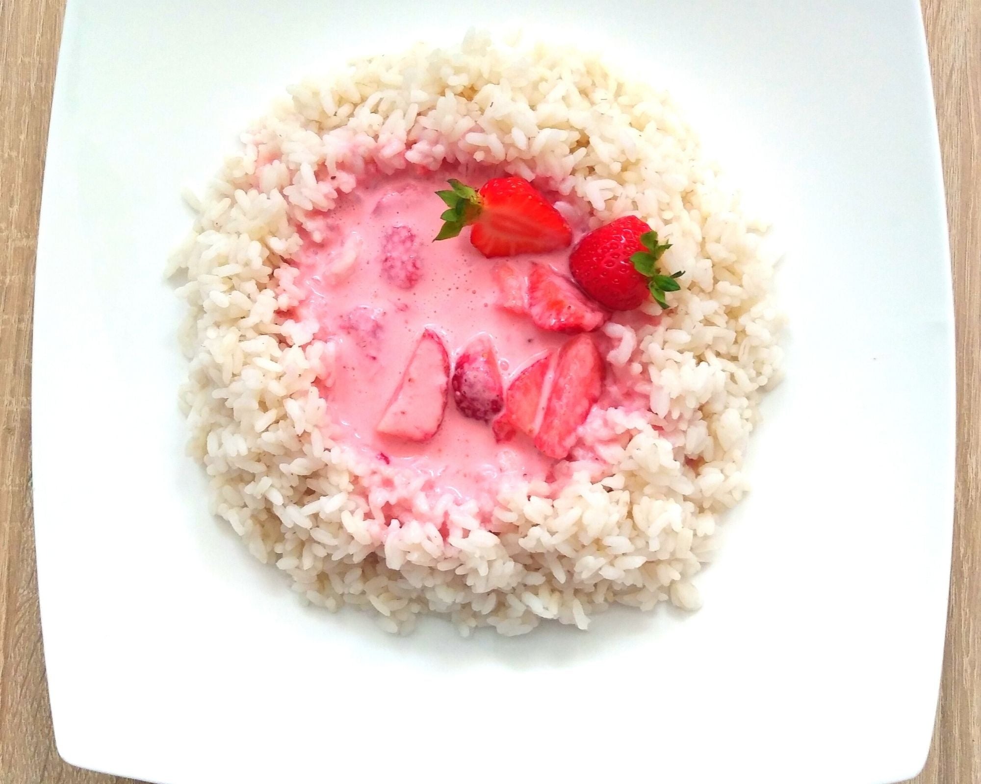 Ryż na mleku z truskawkami, podany na białym talerzu, widok z góry, oświetlenie dzienne.