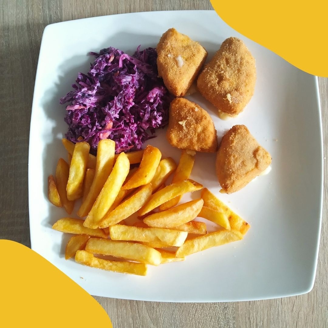 Biały kwadratowy talerz z porcją smażonego sera, frytek i surówki z czerwonej kapusty, ułożonych na drewnianym stole.