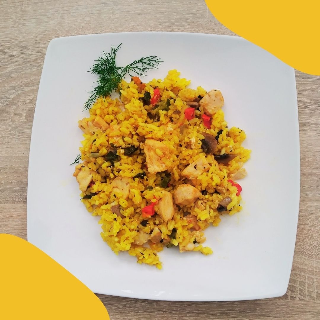 Żółte risotto z kurczakiem, papryką i grzybami, udekorowane gałązką koperku na kwadratowym, białym talerzu, ustawionym na drewnianym blacie.