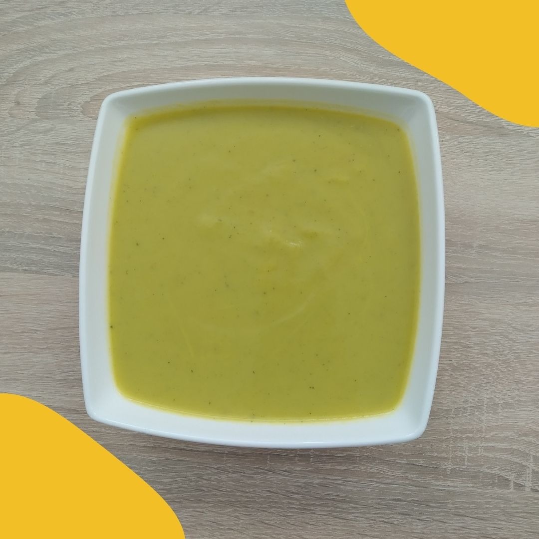 Krem z zielonych warzyw w białym, kwadratowym talerzu na drewnianym stole z żółtymi akcentami w tle.