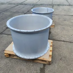 Dwa szare, metalowe cylindry z kołnierzami na paletach, widoczne ślady spawania i mocowania śrubami, na tle betonowego placu.