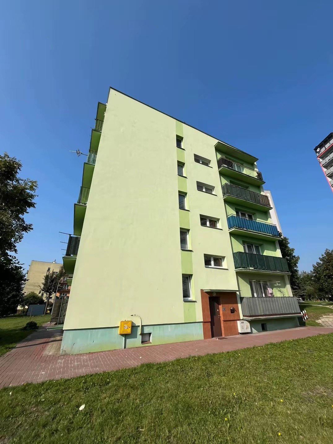 Odświeżona elewacja bloku mieszkalnego w Skarżysku-Kamiennej, widok z dołu na jasnozieloną ścianę i balkony z niebieskimi akcentami, po renowacji.