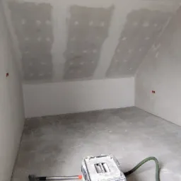 Poddasze po montażu płyt gipsowo-kartonowych, widoczne łączenia szpachlowane. Na podłodze odkurzacz przemysłowy z zielonym wężem.