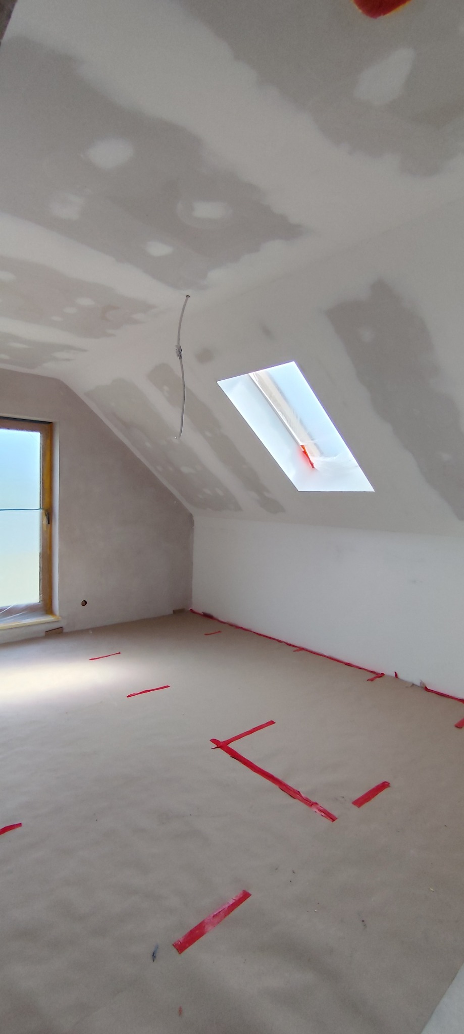 Poddasze po szpachlowaniu, przygotowane do dalszych prac wykończeniowych. Widoczne okno dachowe i zabezpieczona podłoga.