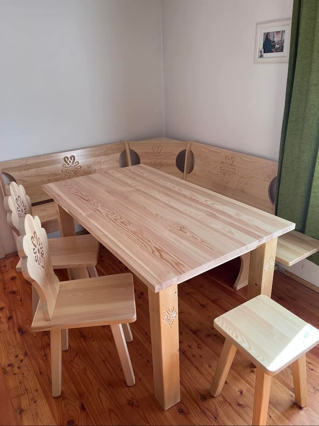 Drewniany stół z krzesłami i narożną ławą w jasnym odcieniu drewna, zdobione motywami kwiatowymi, na drewnianej podłodze.
