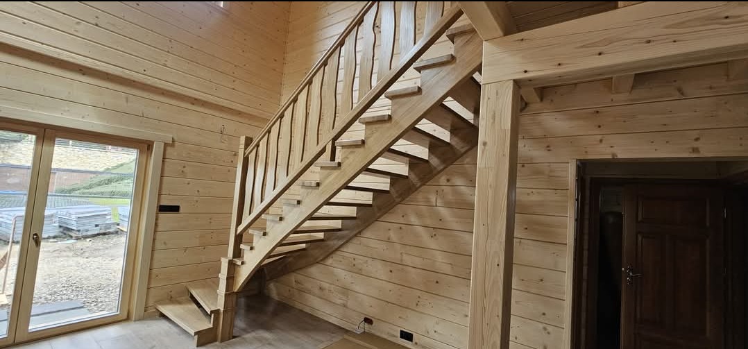 Drewniane schody z balustradą w domu z bali, Rzeszów. Widoczne wykończenie ścian drewnem i drzwi. Naturalne oświetlenie.