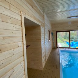 Konstrukcje Drewniane Błażej Gregus - Wnętrze drewnianego budynku z basenem krytym, widok na zewnątrz przez duże okno.