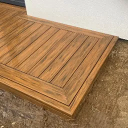 Narożny fragment tarasu z desek kompozytowych, widoczne ślady wilgoci na powierzchni, surowy grunt w tle.