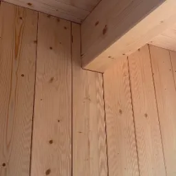 Wnętrze domu w trakcie budowy, widoczne drewniane panele ścienne i belka stropowa z jasnego drewna, charakterystyczne sęki i usłojenie.