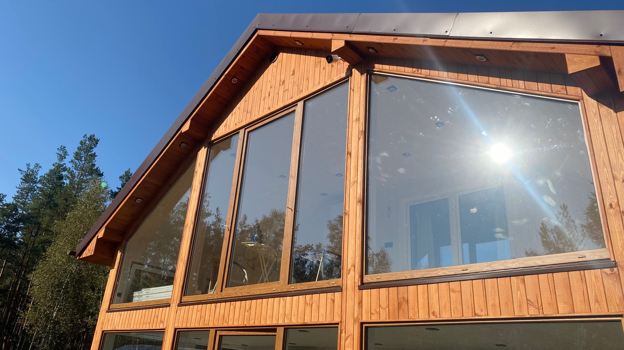 Nowoczesny dom z drewna z dużymi oknami, widok z zewnątrz na elewację i fragment dachu, błękitne niebo w tle.