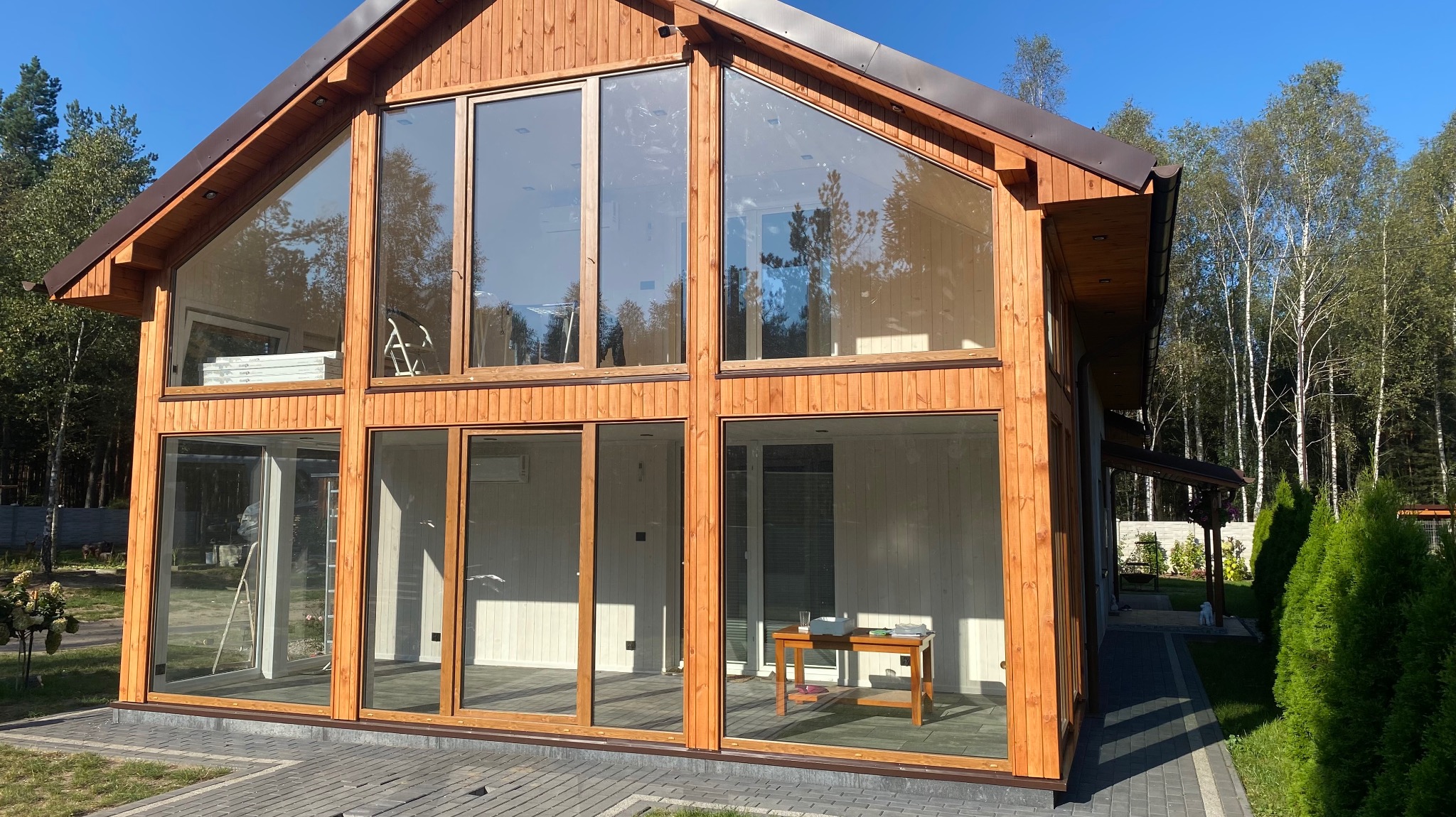 Nowoczesny dom z drewna z dużymi przeszkleniami, widoczne wnętrze z minimalistycznym wyposażeniem, otoczenie leśne.