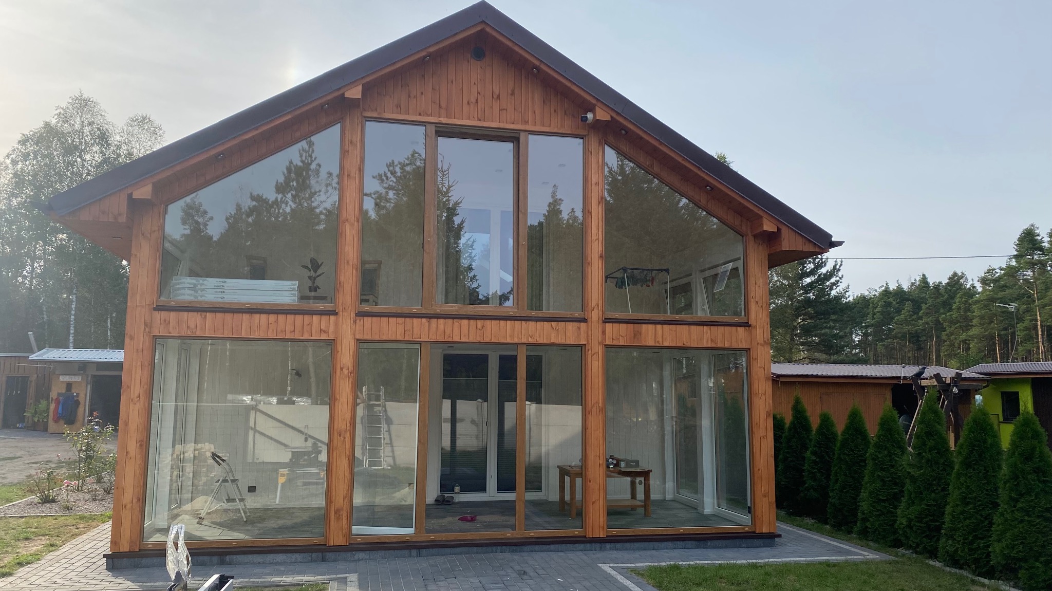 Nowoczesny dom z drewnianą konstrukcją szkieletową i dużymi przeszkleniami, widok z zewnątrz na tle drzew.