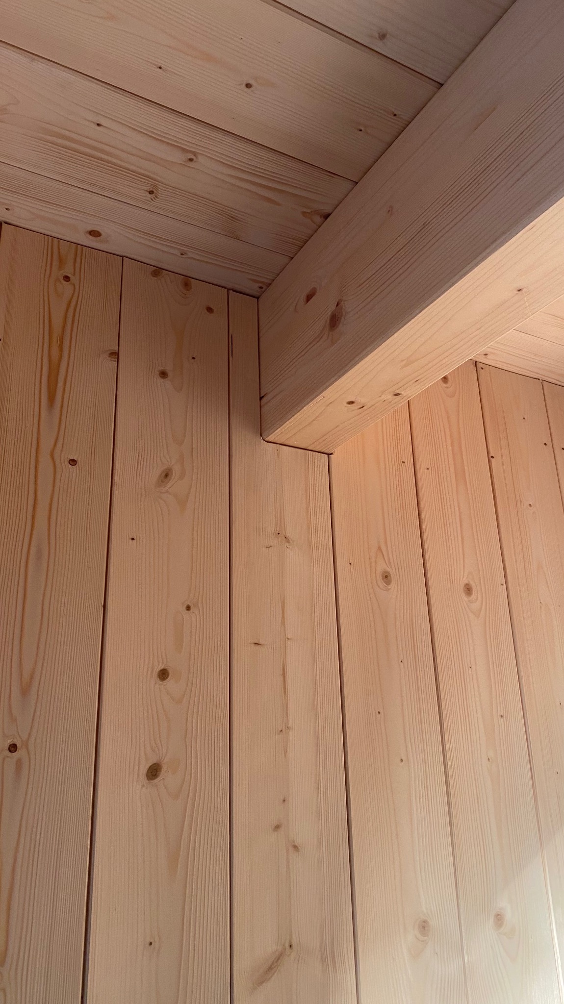 Wnętrze domu w trakcie budowy, widoczne drewniane panele ścienne i belka stropowa z jasnego drewna, charakterystyczne sęki i usłojenie.