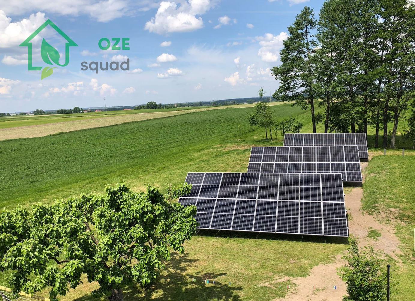 Rząd paneli słonecznych na zielonym polu, widok z lekkiej góry, logo firmy OZE squad w lewym górnym rogu.