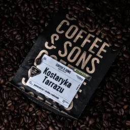Opakowanie kawy ziarnistej Coffee & Sons Kostaryka Tarrazu leży na tle rozsypanych ziaren kawy. Etykieta informuje o nutach smakowych pomarańczy i słodkiej czekolady.