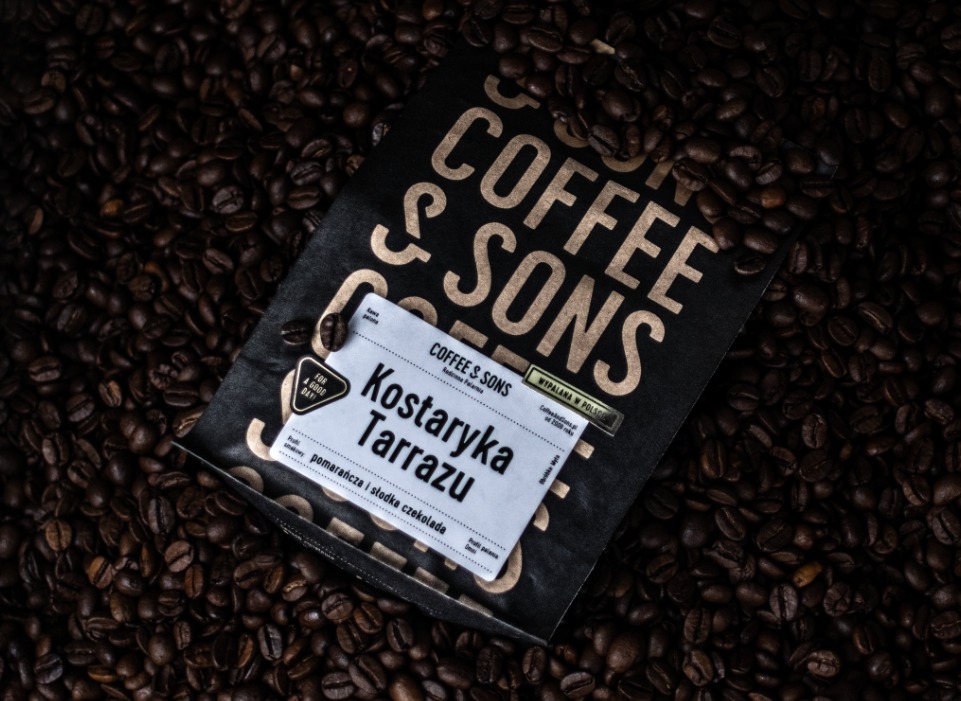 Opakowanie kawy ziarnistej Coffee & Sons Kostaryka Tarrazu leży na tle rozsypanych ziaren kawy. Etykieta informuje o nutach smakowych pomarańczy i słodkiej czekolady.