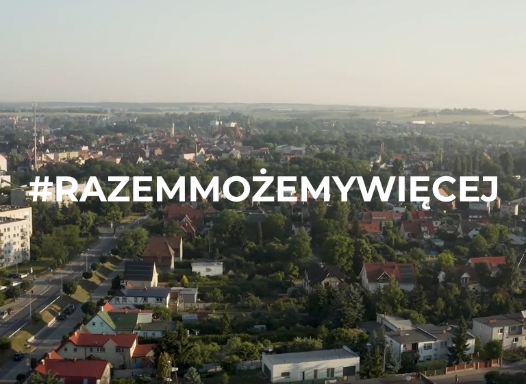 Panorama miasta z lotu ptaka w porannym świetle, z hasłem #RAZEMMOŻEMYWIĘCEJ na pierwszym planie.