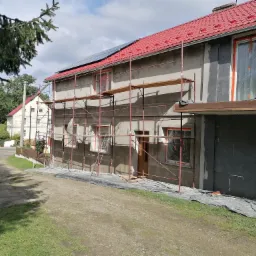 Dom w Włodarach w trakcie prac elewacyjnych z użyciem rusztowania, widoczne ocieplenie oraz folia zabezpieczająca okna.